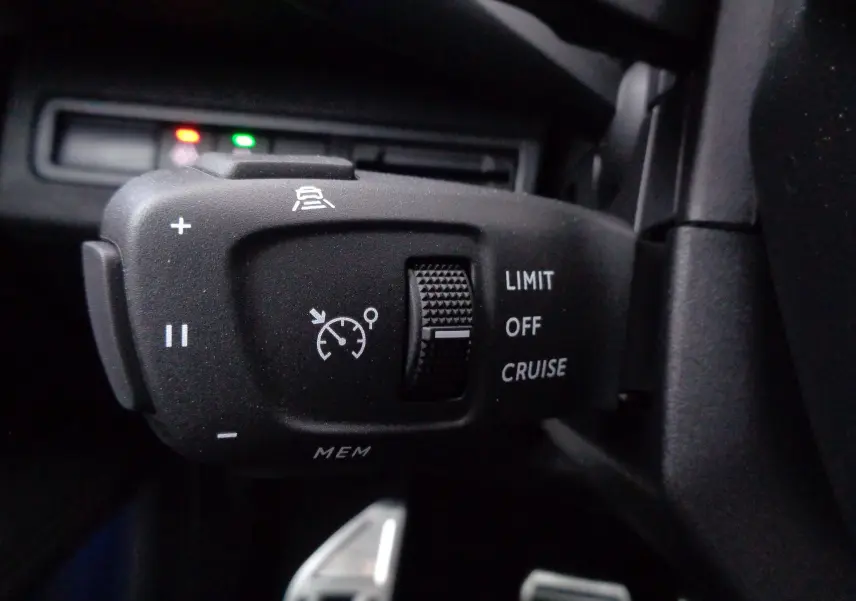 Gros plan sur la commande de régulateur de vitesse du Peugeot 3008 gris, avec molette et symboles blancs visibles.