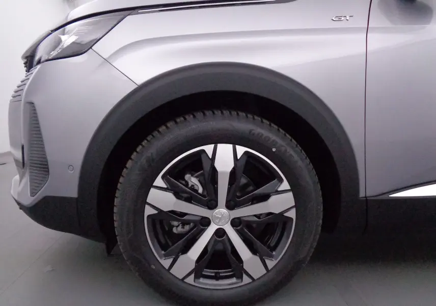 Gros plan sur la roue avant gauche et l'aile gris Artense métallisé du Peugeot 3008 GT 2023 avec logo GT visible.