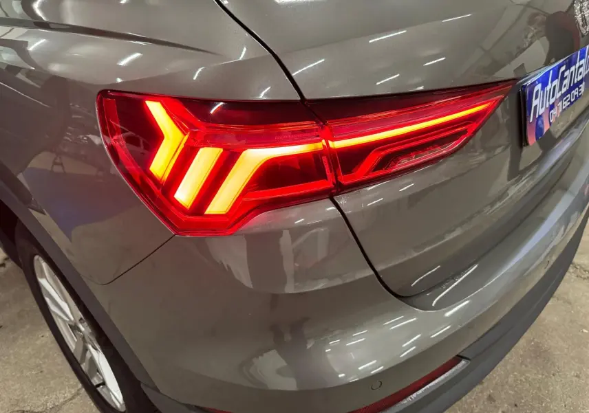 Gros plan sur le feu arrière droit allumé d'un Audi Q3 Business gris, avec partie de la roue et du pare-chocs visibles.