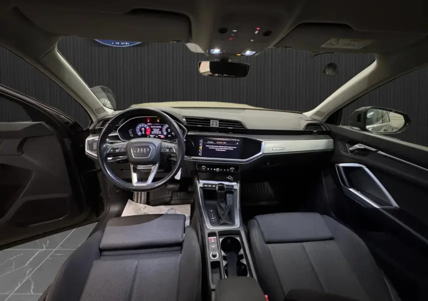 Vue intérieure avant de l'Audi Q3 Business 2019, avec tableau de bord moderne et sellerie tissu gris foncé.