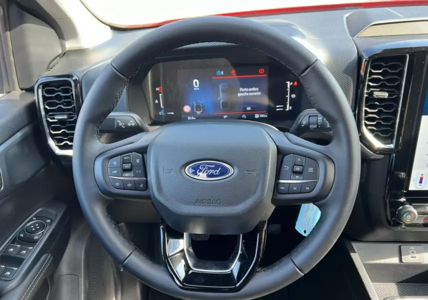 Vue rapprochée du volant cuir multifonctions noir du Ford Ranger 2025 avec tableau de bord numérique et commandes intégrées.