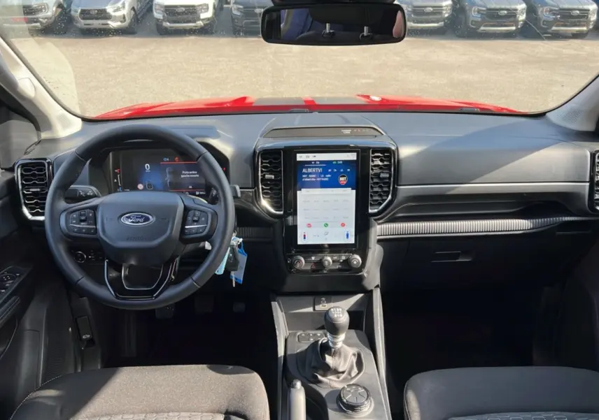 Vue intérieure avant du Ford Ranger rouge racing 2025, volant multifonctions, écran tactile vertical et boîte manuelle.