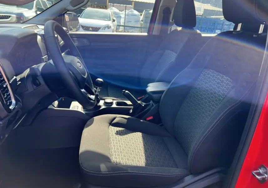 Vue intérieure côté conducteur du Ford Ranger rouge racing 2025, montrant sièges, volant cuir et levier de vitesse manuel.