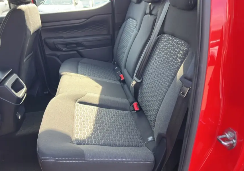 Vue latérale des sièges arrière noirs du Ford Ranger rouge racing 2025, avec ceinture de sécurité et porte ouverte.