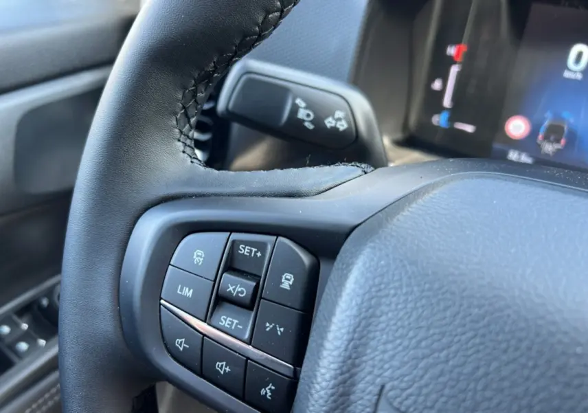 Gros plan sur le volant cuir multifonctions du Ford Ranger 2025, avec commandes de régulateur et tableau de bord numérique flou en arrière-plan.