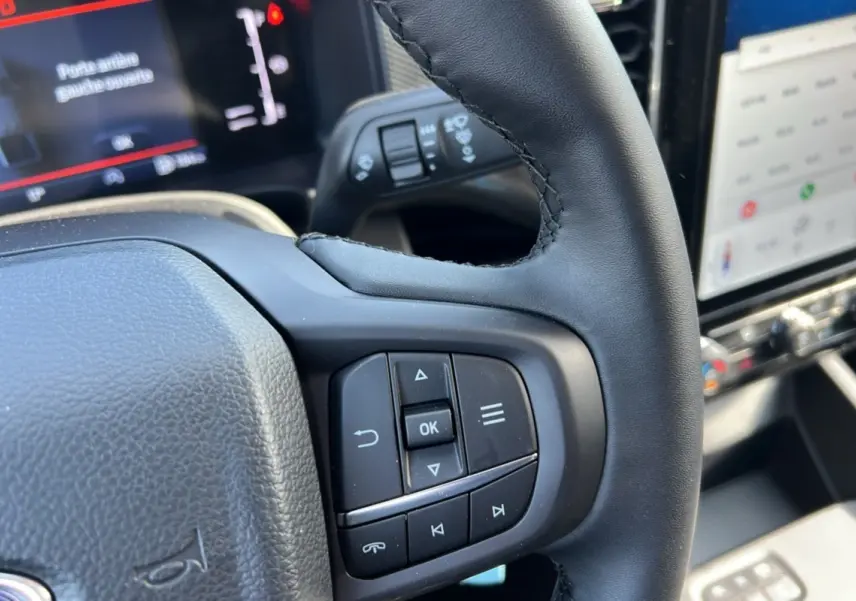 Gros plan sur le volant cuir multifonctions du Ford Ranger 2025 avec commandes intégrées et écran tactile en arrière-plan.