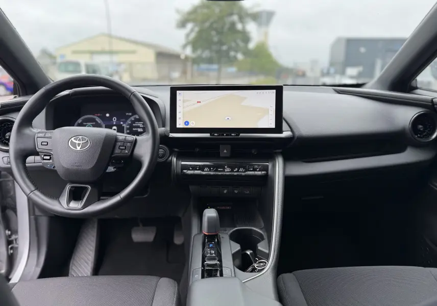 Vue intérieure avant du Toyota C-HR Hybride gris 2024, avec tableau de bord numérique et écran tactile central.