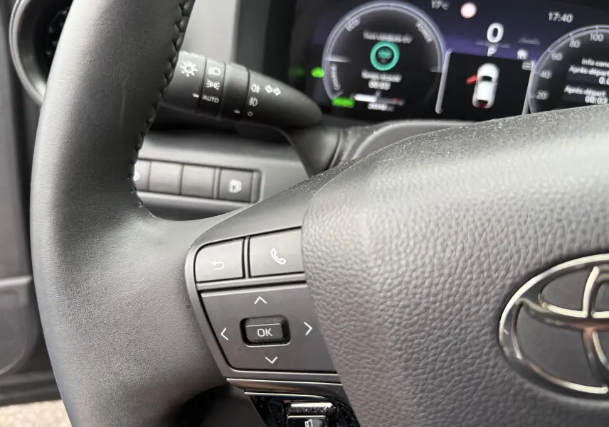 Gros plan sur le volant noir et le tableau de bord numérique du Toyota C-HR Hybride 2024, affichage des commandes au volant.