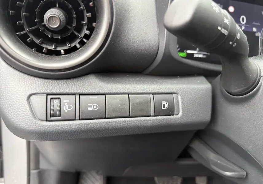 Détail intérieur du tableau de bord côté gauche du Toyota C-HR Hybride gris, avec commandes d'éclairage et bouton de réservoir.