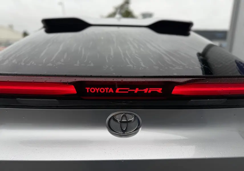 Vue arrière rapprochée du Toyota C-HR hybride gris 2024 avec logo et feux arrière rouges allumés.