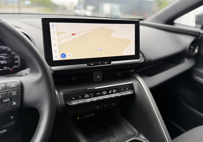 Vue intérieure du tableau de bord du Toyota C-HR Hybride 2024, écran tactile central avec navigation et commandes climatisation digitales.