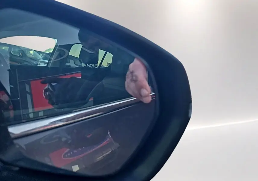Reflet dans le rétroviseur droit d'une Citroën C5 Aircross gris platinium montrant la porte arrière et une main posée dessus.