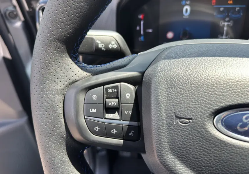 Gros plan sur le volant cuir perforé du Ford Ranger gris carbone, avec commandes multifonctions et logo Ford visible.