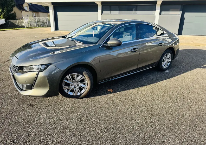 Peugeot 508 gris amazonite vue 3/4 avant droit sur parking, avec jantes alliage et calandre chromée.