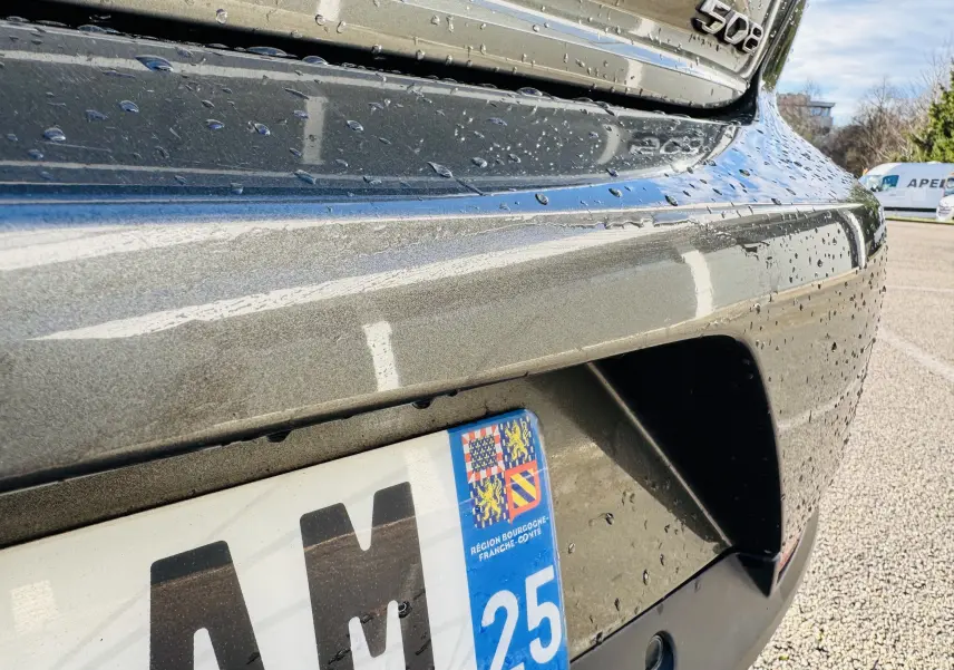 Gros plan sur l’arrière droit gris amazonite d’une Peugeot 508 2019 avec logo et plaque d’immatriculation humide.