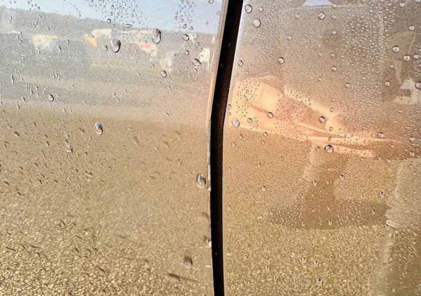 Gros plan sur la portière gris amazonite d'une Peugeot 508, avec gouttes d'eau et reflet flou visible.