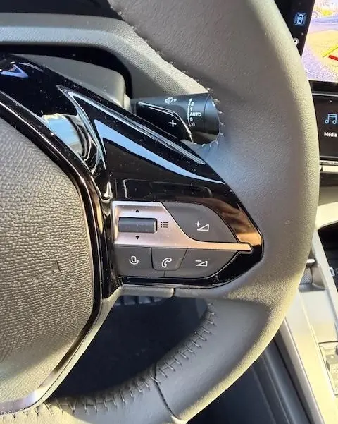 Gros plan sur les commandes multifonctions noires et argent du volant cuir de la Peugeot 308 Hybrid 145 e-DCS6 Allure blanche.