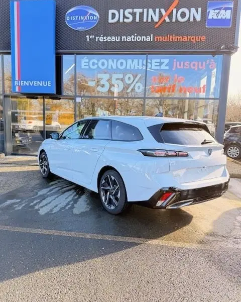 Vue 3/4 arrière droite d'une Peugeot 308 Hybrid blanche stationnée devant une vitrine avec enseigne Distinxion.