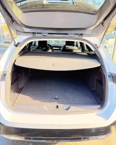 Coffre ouvert vu de l'arrière d'une Peugeot 308 Hybrid 145 e-DCS6 Allure blanche, avec cache-bagages en place.