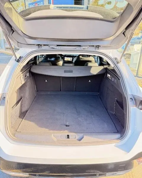 Vue arrière du coffre ouvert d'une Peugeot 308 Hybrid 145 e-DCS6 Allure blanche, montrant l'espace de chargement et la plage arrière.