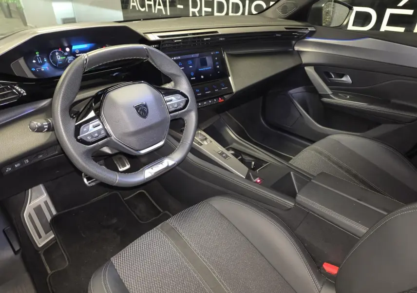 Vue intérieure côté conducteur de la Peugeot 408 GT 2025, tableau de bord noir avec volant cuir perforé et écran tactile central.