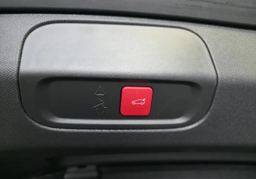 Bouton rouge d'ouverture électrique du hayon sur panneau intérieur noir d'une Peugeot 408 gris Selenium 2025.