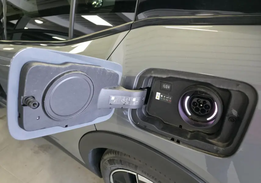 Prise de recharge ouverte côté gauche arrière d’une Peugeot 408 gris métallisé, avec jante alliage 19 pouces visible.