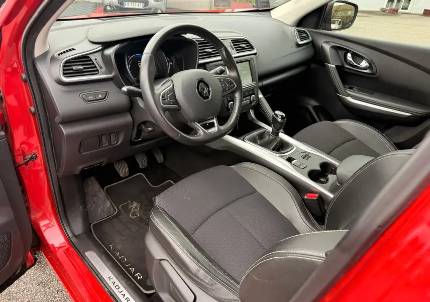 Vue intérieure côté conducteur du Renault Kadjar rouge flamme 2016, avec volant multifonctions et boîte manuelle.