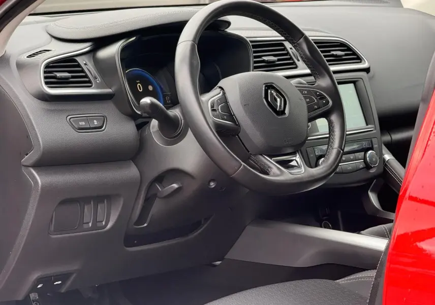 Vue intérieure côté conducteur du Renault Kadjar rouge flamme, mettant en valeur le volant et le tableau de bord digital.