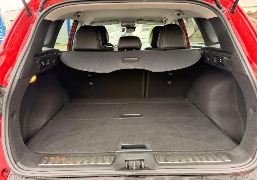 Vue arrière ouverte du coffre spacieux du Renault Kadjar rouge flamme, avec cache-bagages et sièges noirs visibles.