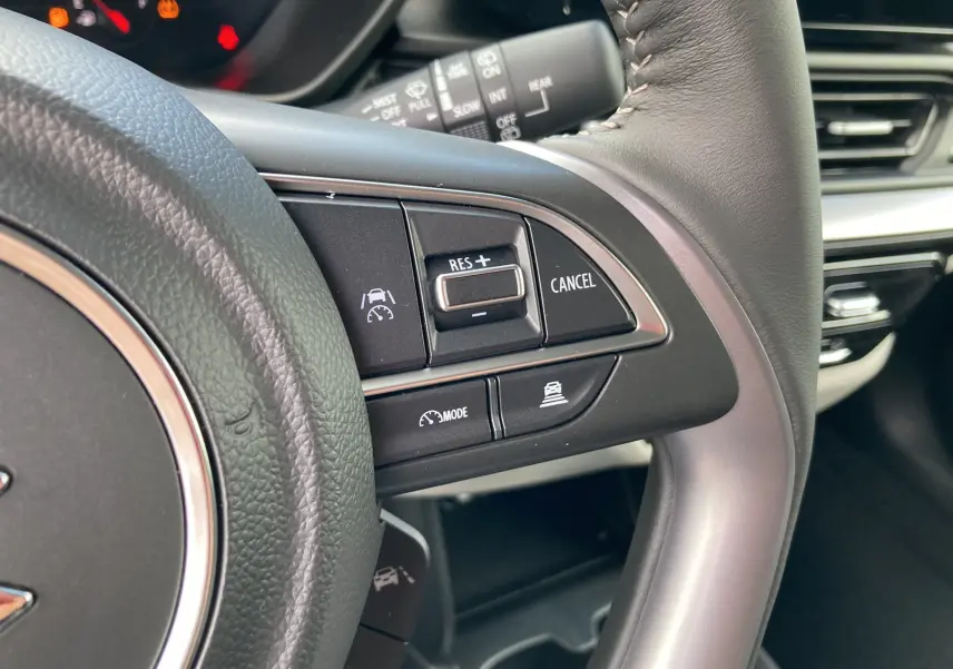 Gros plan sur les commandes multifonctions du volant cuir de la Suzuki Swift 2025, version hybride blanche.