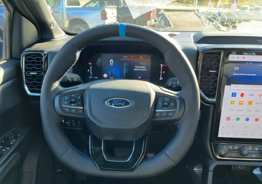 Vue centrée sur le volant cuir noir avec surpiqûres bleues du Ford Ranger 2026, tableau de bord et écran tactile visibles.