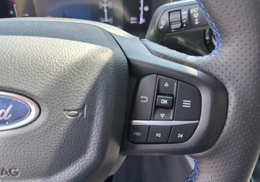 Gros plan sur le volant cuir perforé avec surpiqûres bleues du Ford Ranger gris carbone, boutons multifonctions visibles.