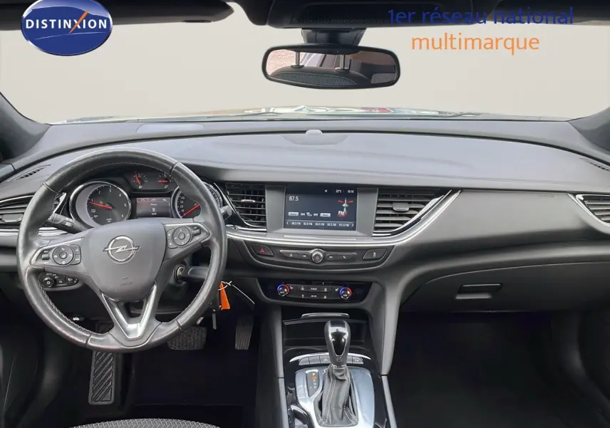 Vue intérieure de face du tableau de bord et volant d'une Opel Insignia Sports Tourer gris acier satinée, avec écran central et boîte automatique.