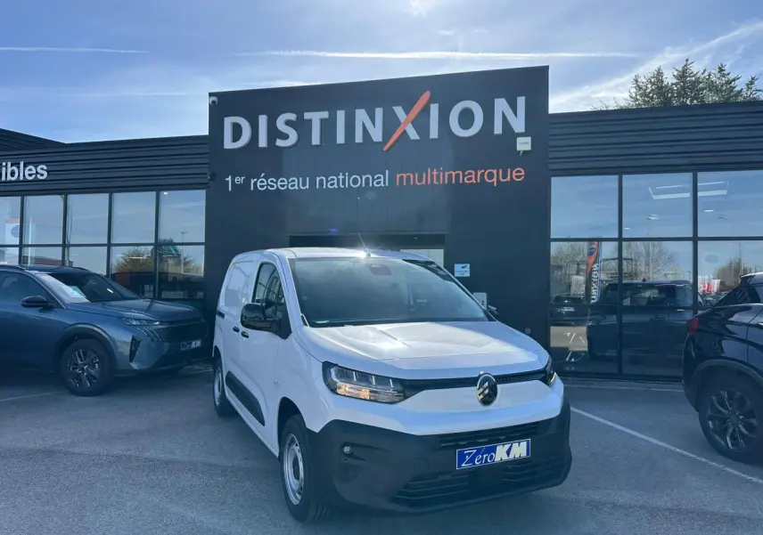 Vue 3/4 avant d'un Citroën Berlingo blanc Icy avec calandre noire, stationné devant un showroom Distinxion.
