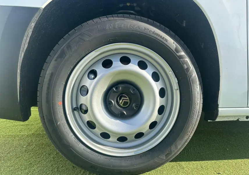 Gros plan sur la roue avant gauche en jante tôle grise du Citroën Berlingo blanc Icy, avec pneu noir visible.