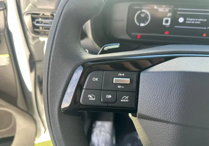 Gros plan sur les commandes à gauche du volant noir du Citroën Berlingo blanc, avec tableau de bord numérique en arrière-plan.