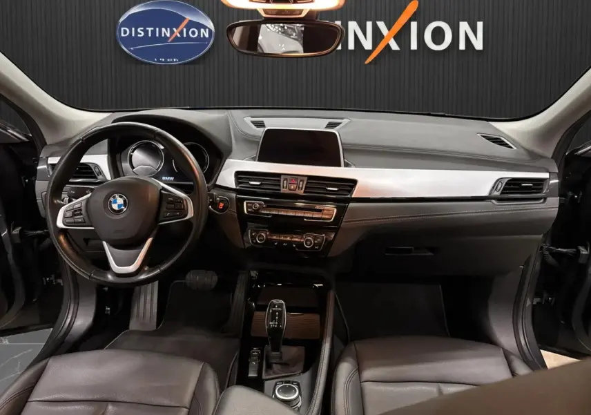 Vue intérieure avant du BMW X2 2019 montrant le tableau de bord noir, le volant cuir et la console centrale avec écran tactile.