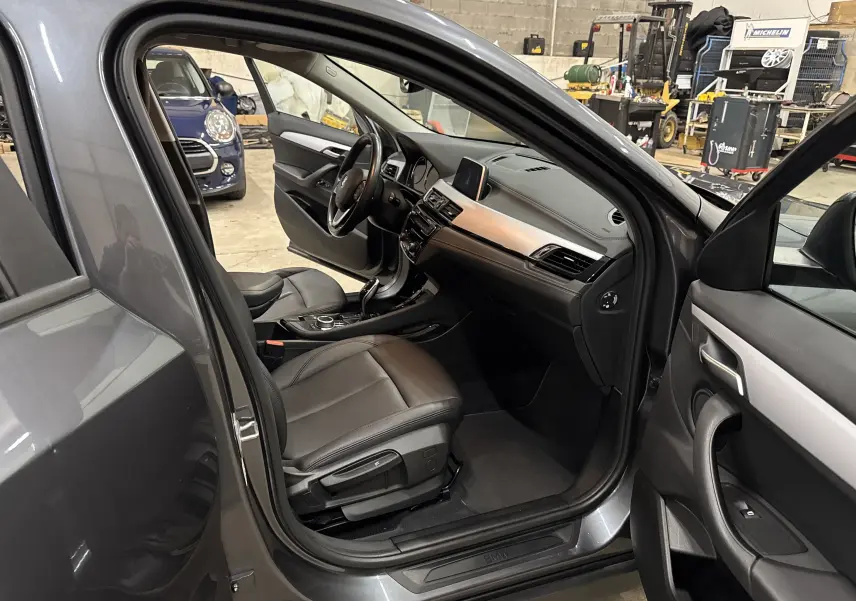 Intérieur noir cuir d'une BMW X2 gris minéral, vue côté gauche avec portes avant et arrière ouvertes, tableau de bord visible.
