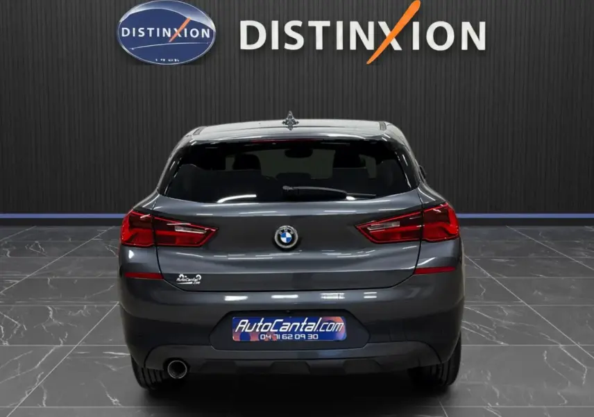 Vue arrière d'une BMW X2 gris minéral métallique 2019, avec hayon fermé et feux arrière allumés en intérieur showroom.