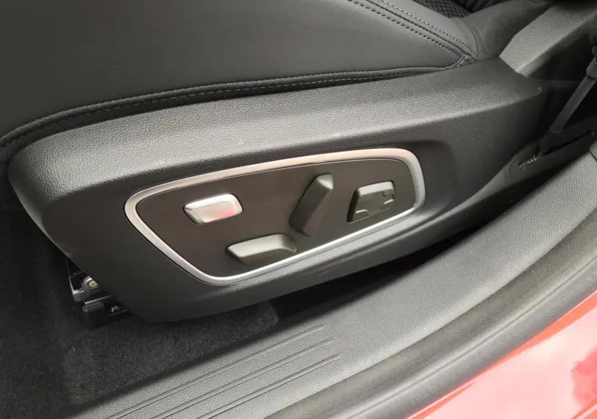 Détail des commandes électriques du siège conducteur noir avec surpiqûres, seuil de porte rouge métallisé bi-ton.