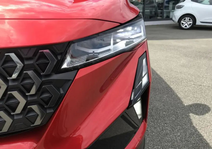Gros plan sur l'avant droit rouge et noir du Renault Austral 2025, mettant en valeur le phare LED et la calandre hexagonale.