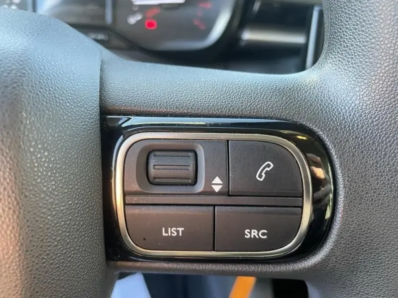 Gros plan sur les commandes multifonctions du volant d’une Citroën C3 gris foncé, avec boutons list, SRC et téléphone.