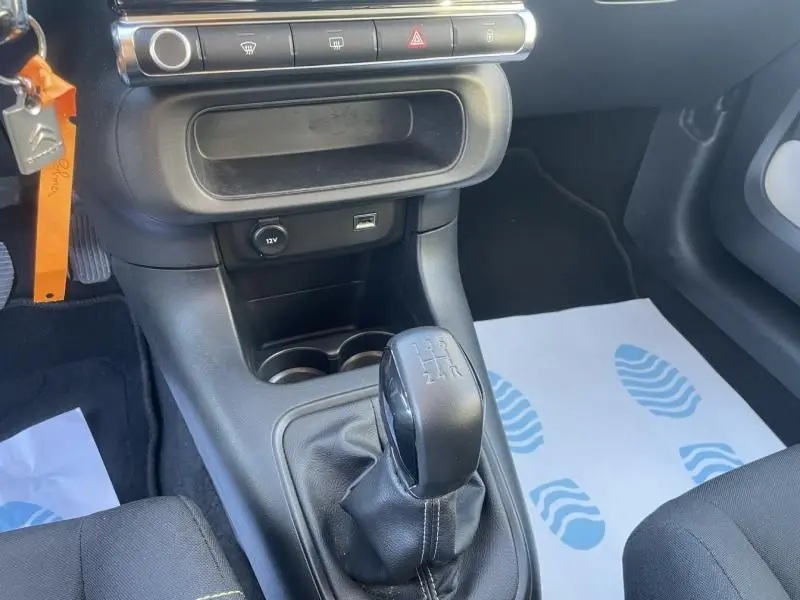 Vue intérieure centrée sur le levier de vitesse manuel noir du Citroën C3 gris foncé, avec console et prises USB visibles.
