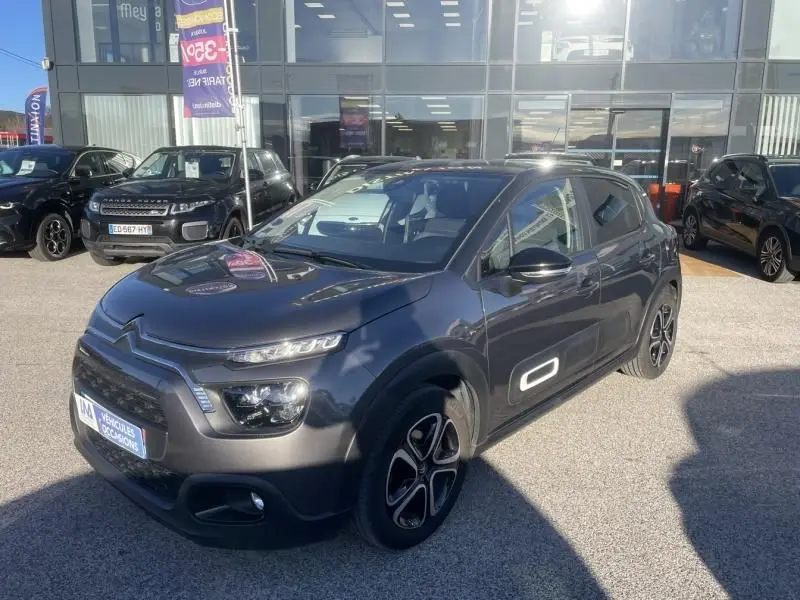 Citroën C3 gris foncé vue 3/4 avant droit, avec détails Airbump blancs sur les portières, stationnée devant un showroom.