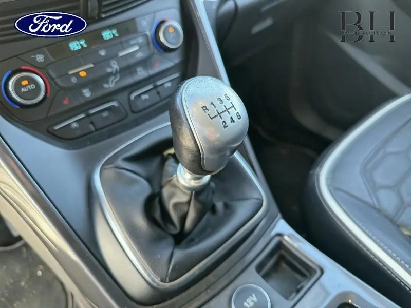 Gros plan sur le levier de vitesse manuel en cuir noir du Ford Kuga blanc, avec console centrale et sièges partiellement visibles.