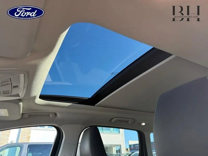 Vue intérieure du toit ouvrant panoramique électrique du Ford Kuga blanc, avec ciel bleu visible à travers le verre.