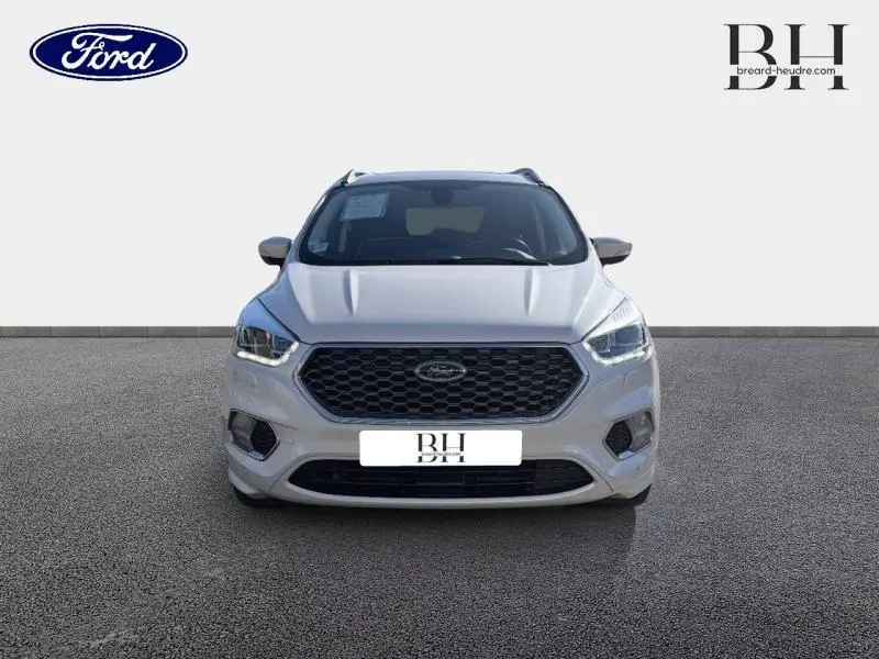 Vue avant d'un Ford Kuga blanc Premium Platinum avec calandre hexagonale noire et phares halogènes allumés.