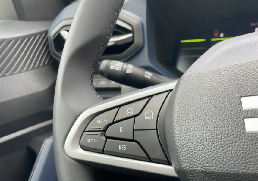 Gros plan sur les commandes au volant cuir du DACIA BIGSTER 2025, version gris schiste, côté gauche du volant.