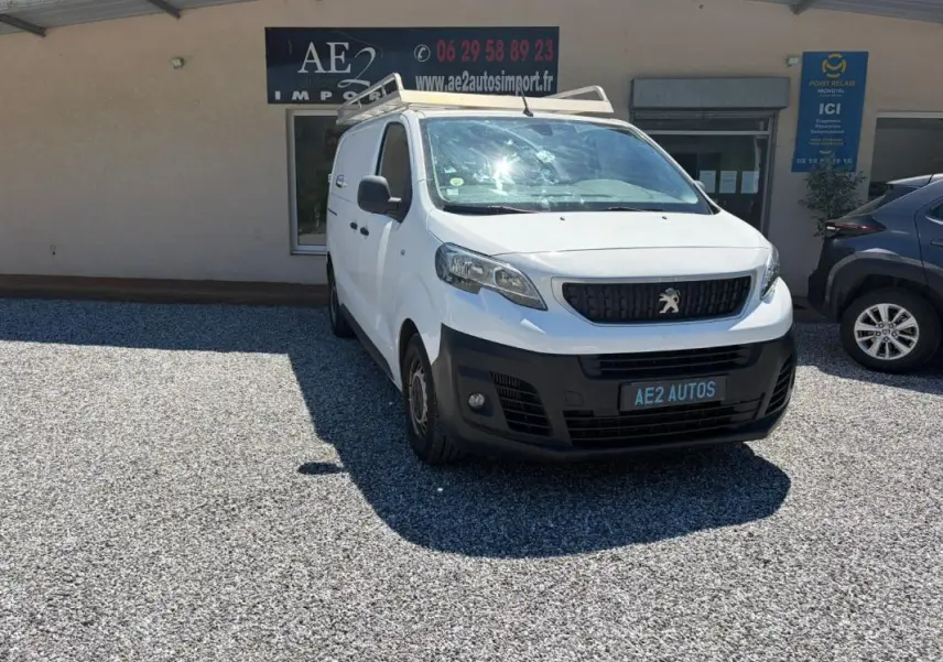 Peugeot Expert Fourgon blanc en 3/4 avant droit avec galerie de toit, stationné devant un bâtiment commercial.